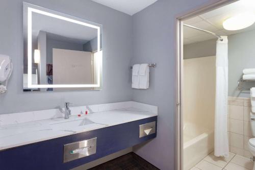 a bathroom with a sink and a mirror and a shower at AmericInn by Wyndham Peoria in Peoria