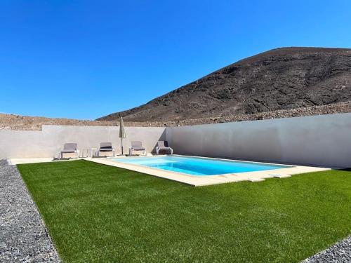 a swimming pool with green grass next to a mountain at Cómoda villa en la montaña in Gran Tarajal