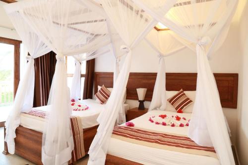 two beds in a bedroom with white drapes at Zanzibar Bahari Villas in Matemwe
