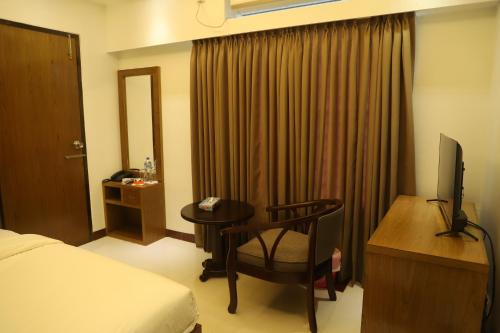 a hotel room with a bed and a desk with a television at Hotel Holy Gate in Sylhet