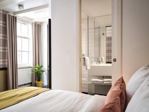 ein Schlafzimmer mit einem Bett und ein Badezimmer mit einem Waschbecken in der Unterkunft Max Brown Hotel Canal District, part of Sircle Collection in Amsterdam