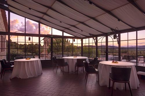 un restaurante con mesas y sillas blancas y ventanas en The Club House, en Castelnuovo Berardenga