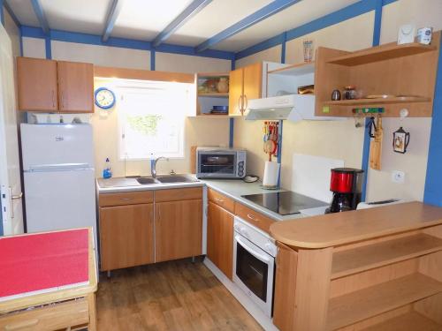 Elle comprend une petite cuisine avec des placards en bois et un réfrigérateur blanc. dans l'établissement La Tremblade - DECOUVREZ ce MOBIL-HOME sur un TERRAIN PRIVE, à La Tremblade