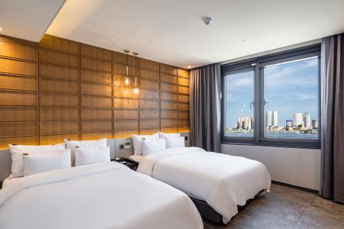 two beds in a hotel room with a window at Sokcho Business Hotel CAMEL in Sokcho