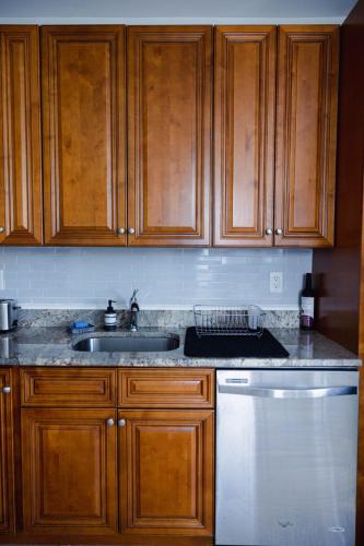 a kitchen with wooden cabinets and a white dishwasher at Rainforest Retreat 20m to NYC Parking Sleeps 25 in Bayonne