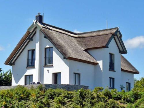 ein weißes Haus mit einem Dach über einigen Büschen in der Unterkunft Reetdachhaus im Fischerdorf in Freest