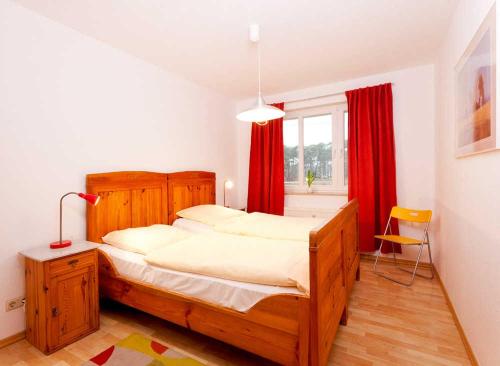 1 dormitorio con cama grande de madera y cortinas rojas en Wohnung 22, en Ostseebad Karlshagen