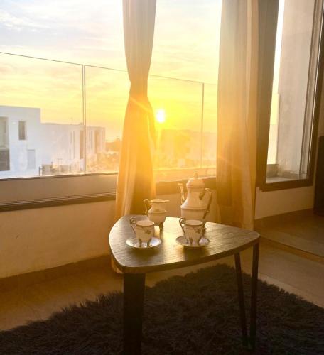 a table with two tea cups on it in front of a window at Apt Raffiné Taghazout Bay Vue Océan luxe 6p in Tamraght Ouzdar