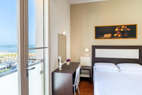 una camera d'albergo con letto, scrivania e finestra di Amare Beach Hotel a Cesenatico