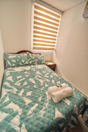 a bed with a green comforter and a pair of shoes on it at Apartamentos Amoblados Confort Turismo en Cúcuta in Cúcuta