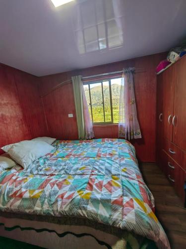 Un dormitorio con una cama con un edredón colorido y una ventana en Entre saltos, en Lonquimay