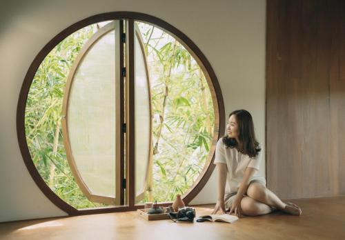 a woman sitting on the floor in front of a large window at InnerZen Riverside homestay Ben Tre - Japanese style in Ấp Phú Hòa (3)
