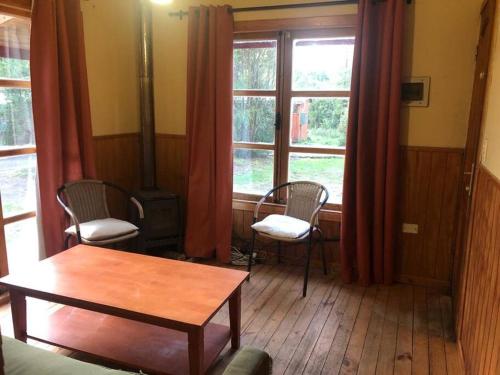 uma sala de estar com 2 cadeiras, uma mesa e janelas em Cabaña Haywood em Puerto Varas