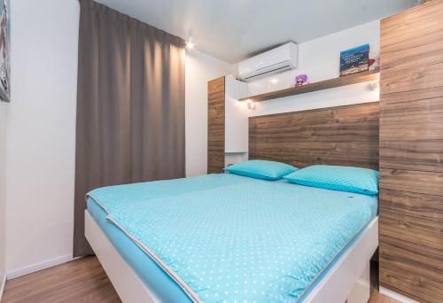 Schlafzimmer mit einem Bett mit einem Kopfteil aus Holz und blauen Kissen in der Unterkunft Mobile Home SIMBA in Biograd na Moru