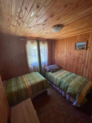 two beds in a room with wooden walls at Cabaña Ojo del Volcán in Pucón