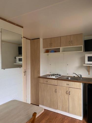 une cuisine avec des armoires en bois, un évier et une table dans l'établissement Mobil-home mitoyen 1 chambre, à Angicourt