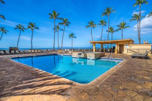 a swimming pool with palm trees and a beach at Sugar Beach Resort in Kihei