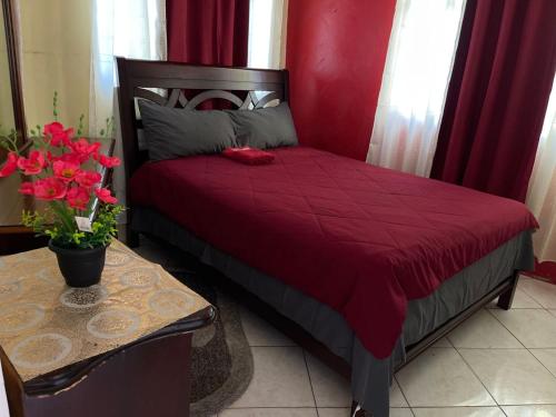 a red bed with a red comforter and a table with flowers at Elite's Ocean View in Montego Bay