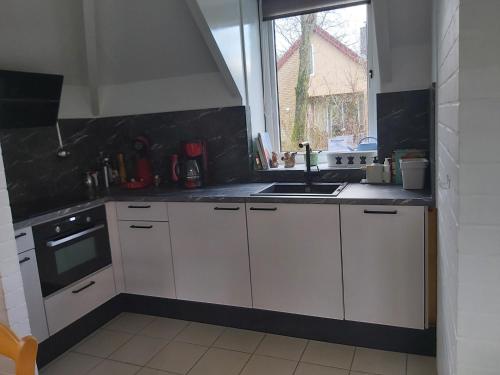uma cozinha com armários brancos, um lavatório e uma janela em ons Bosnest em Dalfsen