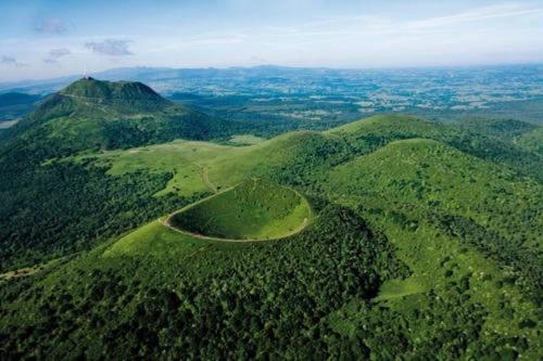 an aerial view of a green mountain with a road at La Loge des Volcans - Vue Puy De Dôme in Saint-Genès-Champanelle