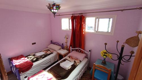 two beds in a room with purple walls and windows at Hôtel Restaurant BOUGAFER in Oulad Akkou