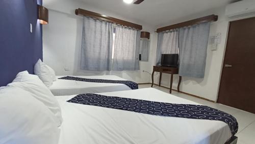 a room with two beds and a television and windows at Hotel Tropical in Progreso