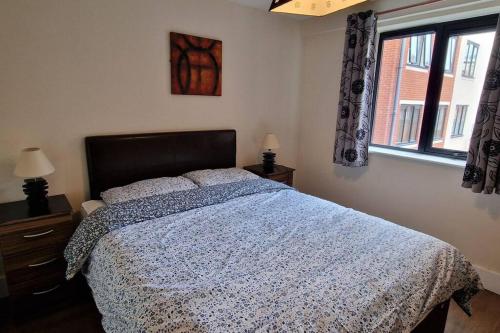 a bedroom with a bed with a blue comforter and a window at 2 Bedroom Apartment Central Birmingham City Centre ( Parking ) in Birmingham