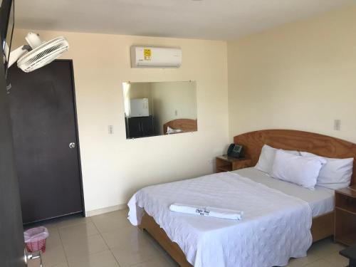 Schlafzimmer mit einem Bett mit weißer Bettwäsche und einem Spiegel in der Unterkunft Coffee Hotel in Planadas