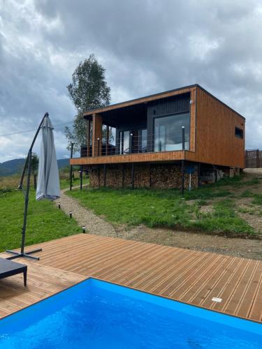 a sustainable house with a pool and an umbrella at Under Sky Slavske - Котеджі з Теплим басейном ,чаном-джакузі, панорамною ванною та PlayStation 5 in Slavske