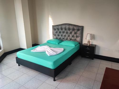 a bedroom with a bed with green sheets and a headboard at La Gran Mansión en el corazón de Pereira in Pereira