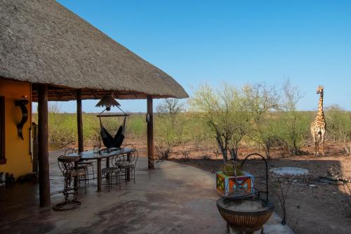 a hut with a table and chairs and a giraffe at Yingwe self catering villa bordering Kruger with private pool in Phalaborwa