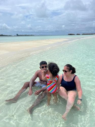 a group of people sitting in the water on a beach at Konut by Thakuru in Guraidhoo