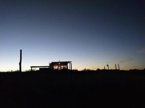 a silhouette of a building in a field at sunset at Mandalei, Refugio De Mar in Las Grutas