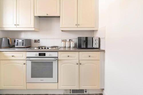 een witte keuken met witte kasten en apparaten bij Immaculate 2-Bed Apartment in Welwyn Garden City in Welwyn Garden City