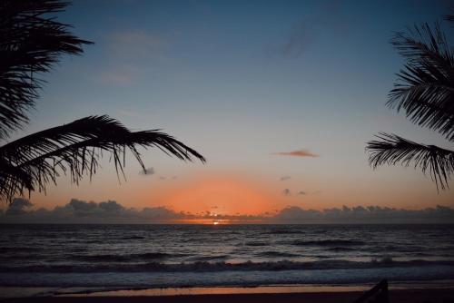 um pôr do sol na praia com palmeiras em Pousada Casa Mar pé na areia em Caraíva