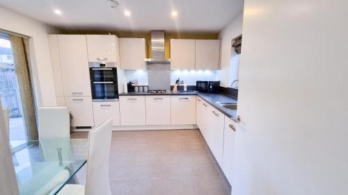 a kitchen with white cabinets and a glass table at Family & Business Stays In RG2 - Sleeps Up to 12! in Reading