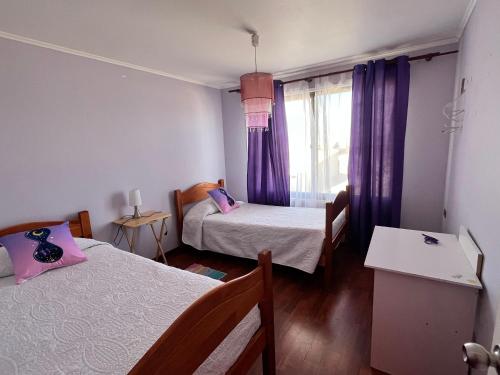 een kamer met 2 bedden en een raam met paarse gordijnen bij Casa Colibrí - Tongoy in Tongoy