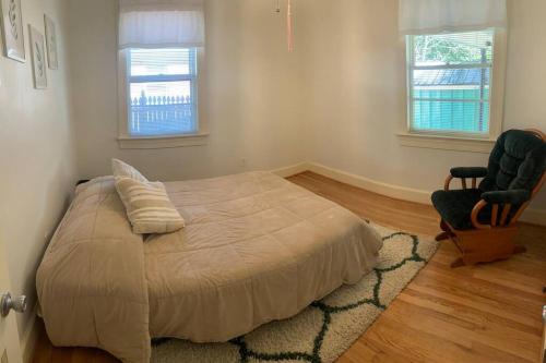 ein Schlafzimmer mit einem Bett und einem Stuhl sowie zwei Fenstern in der Unterkunft Cozy Brick House Mins to Hospital in Goldsboro