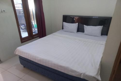 a bed with white sheets and pillows next to a window at SPOT ON 93553 Juan Kostel in Banyumas