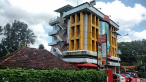 a tall yellow building next to a street at Sap Inn Pallom in Kottayam