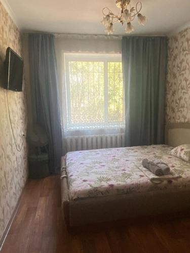 a bedroom with a bed and a window and a television at Тихая теплая уютная однушка in Karagandy