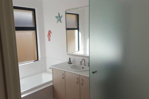 a bathroom with a sink and a tub and a mirror at Southern River Family Accommodation. Free WiFi in Perth