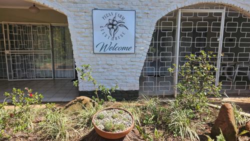 a building with a welcome sign and plants in a yard at Pecan Farm Guesthouse in Louis Trichardt