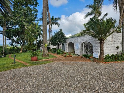 a white house with palm trees and a driveway at Pecan Farm Guesthouse in Louis Trichardt