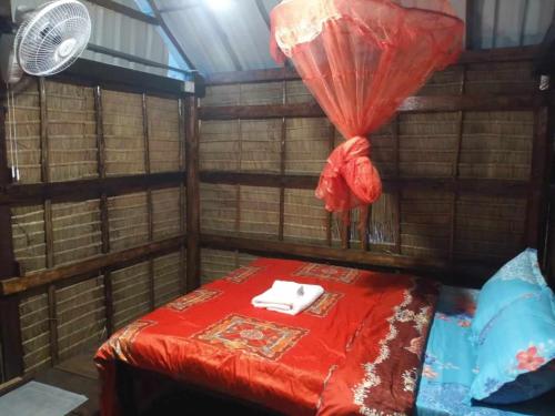 a small room with a red bed with a fan at Le Soleil in Kep