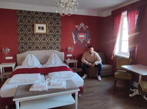 un homme assis dans une pièce rouge avec un lit dans l'établissement Marius Kammer und Koppel Engelbrecht, à Höbersdorf