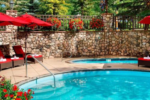 a swimming pool with a stone wall and red umbrellas at Beaver Creek Lodge 510 in Beaver Creek