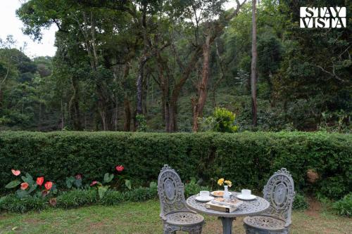 a table with two chairs in front of a hedge at 3BR Mercara Hill Villa with Outdoor Jacuzzi and Complimentary breakfast - Coorg in Madikeri