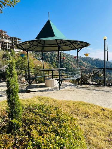 a picnic table with a green umbrella in a park at Green Lodge Farmstay by Highland Monk in Shimla