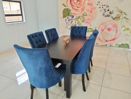 a dining room table with blue chairs and a painting at O&S BnB in Centurion